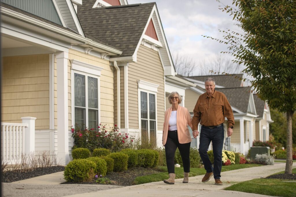 Male and female retiree couple walking outside through personal care community on sunny day