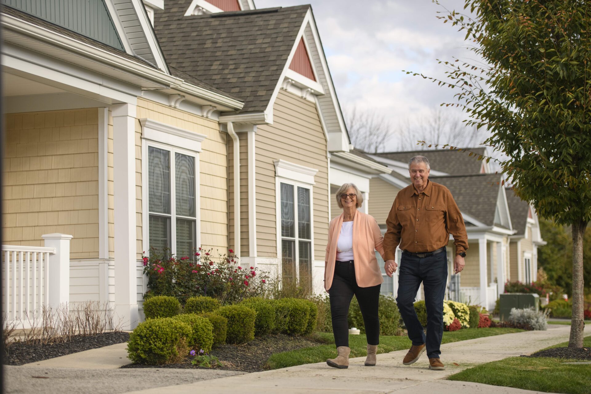 Male and female retiree couple walking outside through personal care community on sunny day