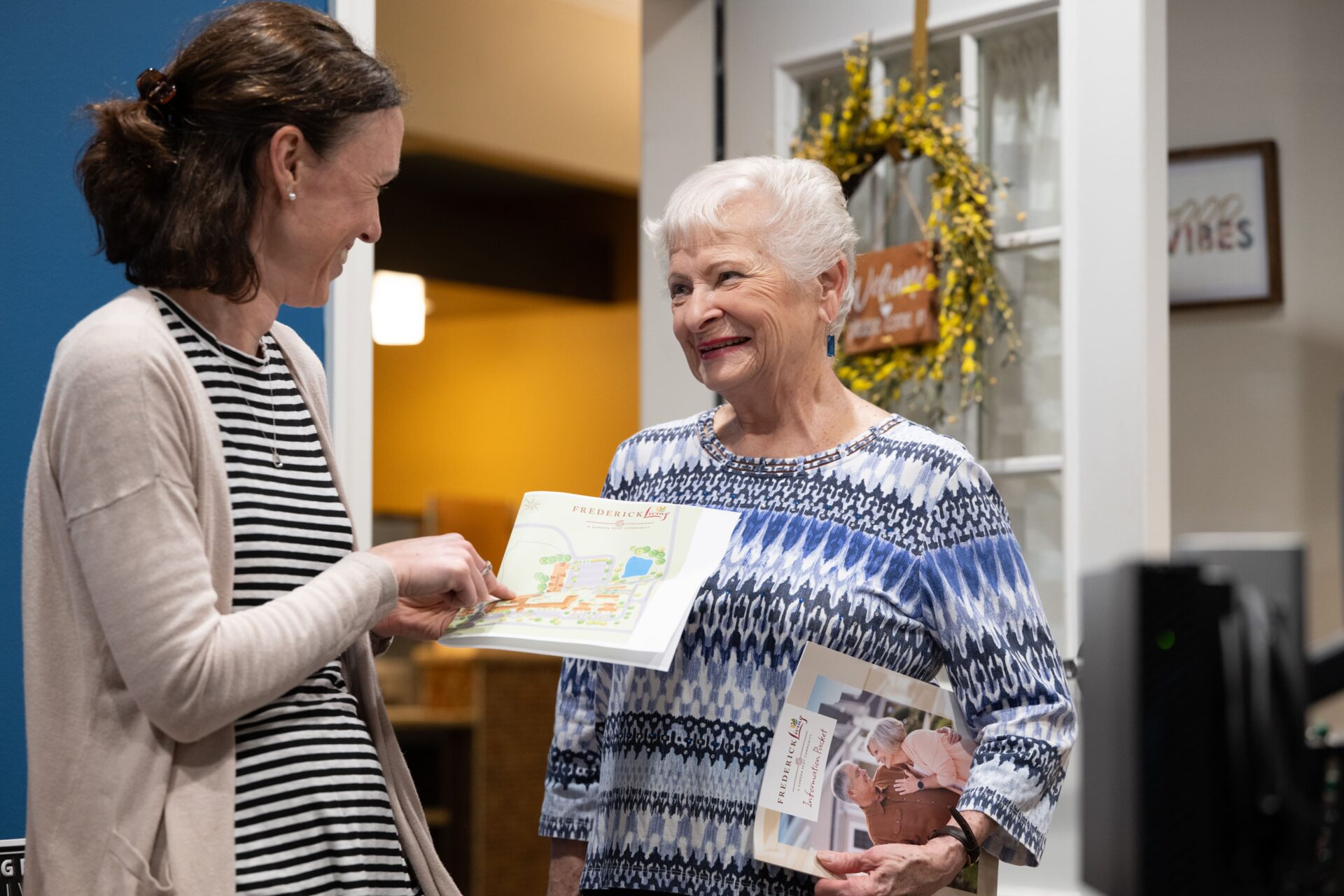 A helpful staff member reviews a community map with a smiling senior woman while discussing memory care services and amenities.