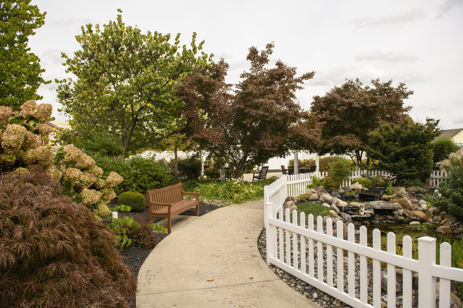 A scenic wooden gazebo and paved walking trail surrounded by trees and a lamp post, highlighting active retirement living with amenities.