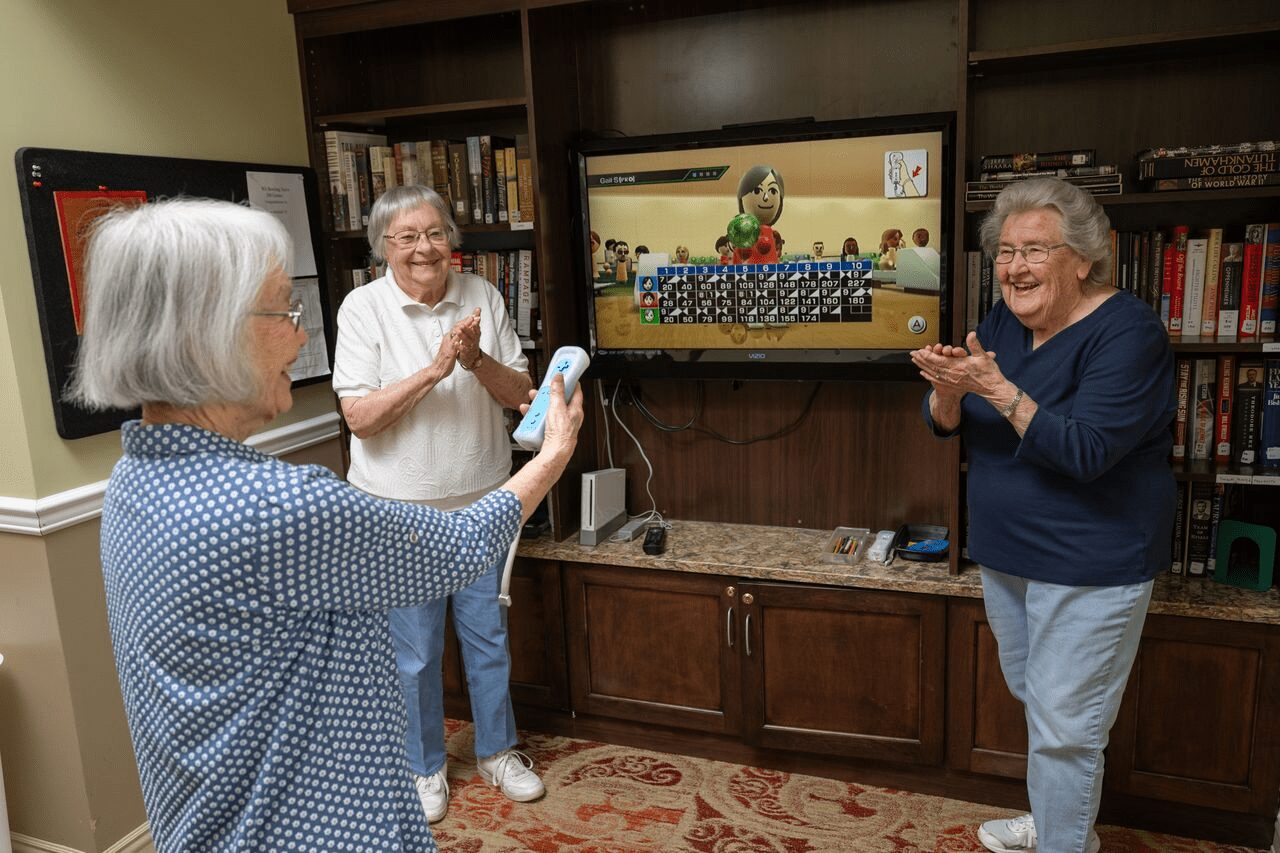 Three women laughing and cheering while playing a Wii bowling video game in the library lounge, enjoying the fun on-site amenities