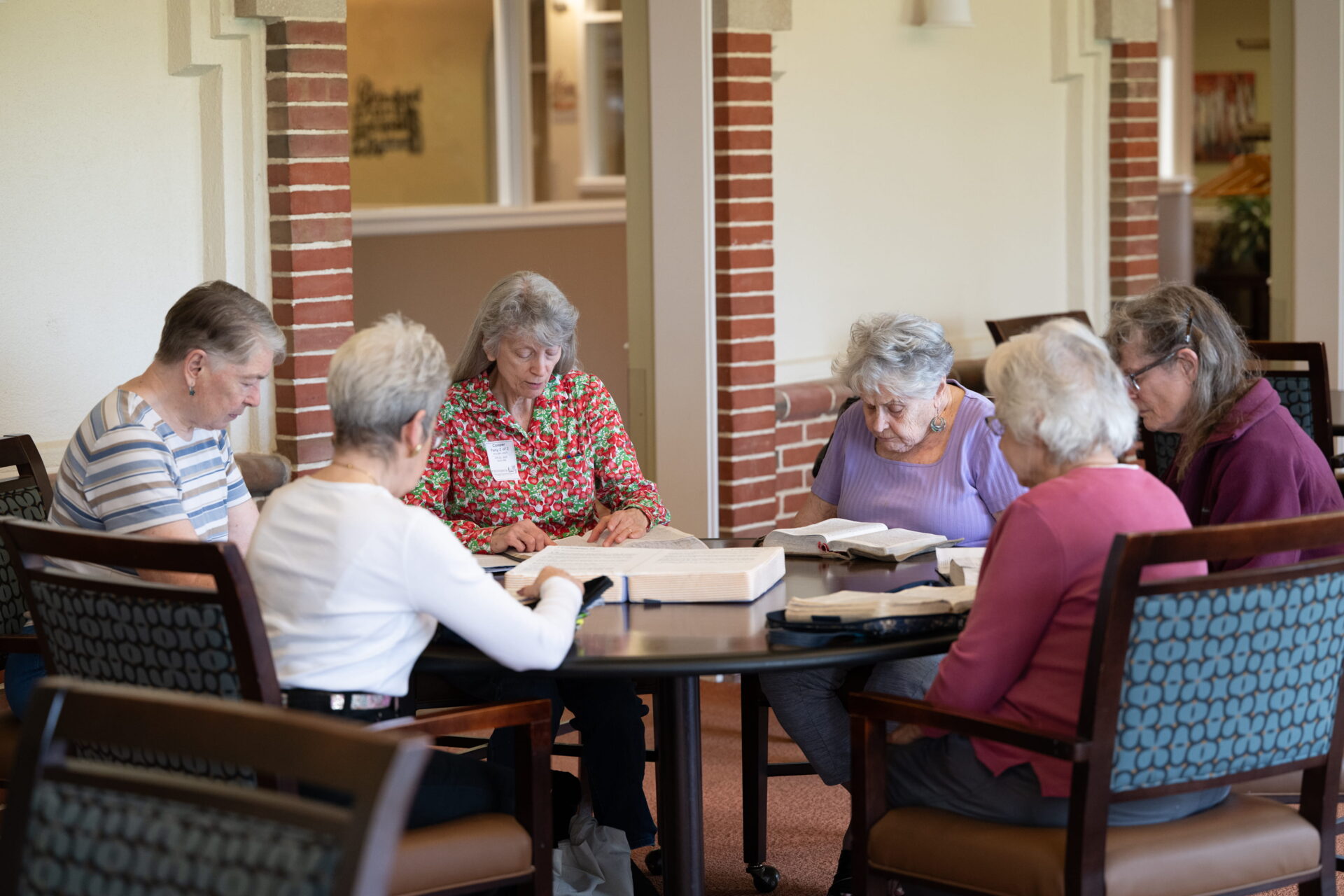 A group of women gathered around a table for a book study in a bright communal space, representing the social engagement supported by various financial plan options.