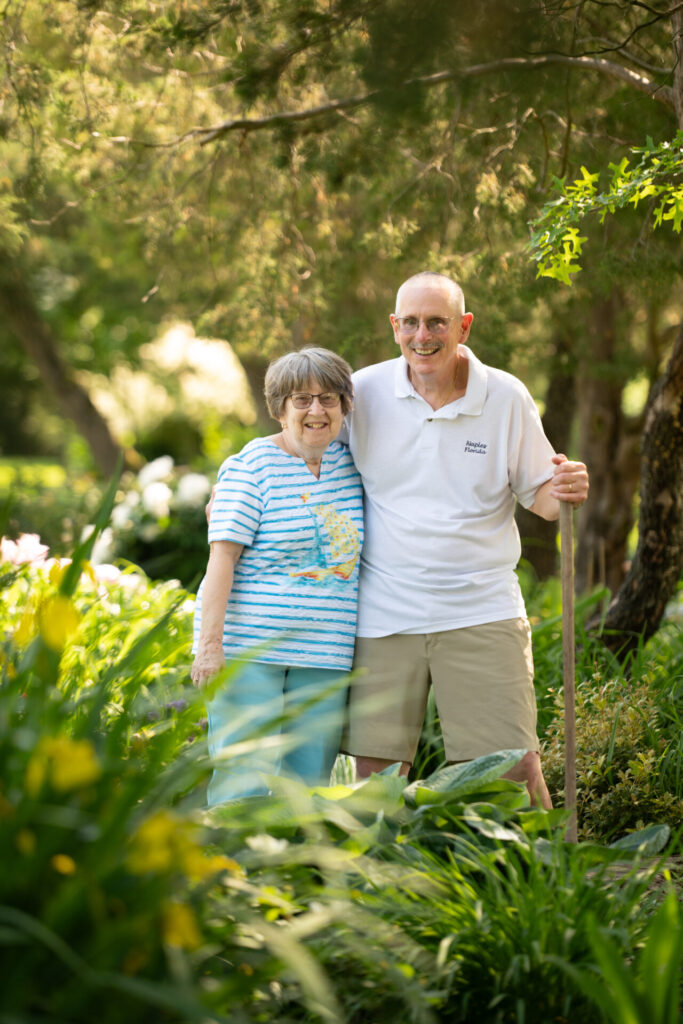 A smiling older couple stands together in a lush green garden, enjoying the beautiful outdoor spaces and peace of mind often found at personal care homes.