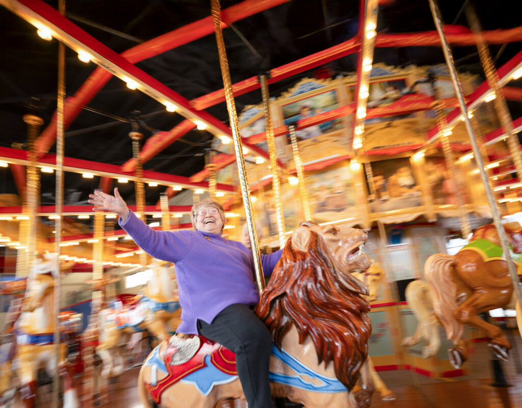 A senior woman smiling widely while riding a carousel, which can inspire important retirement community tour questions regarding off-campus excursions and recreational activities.