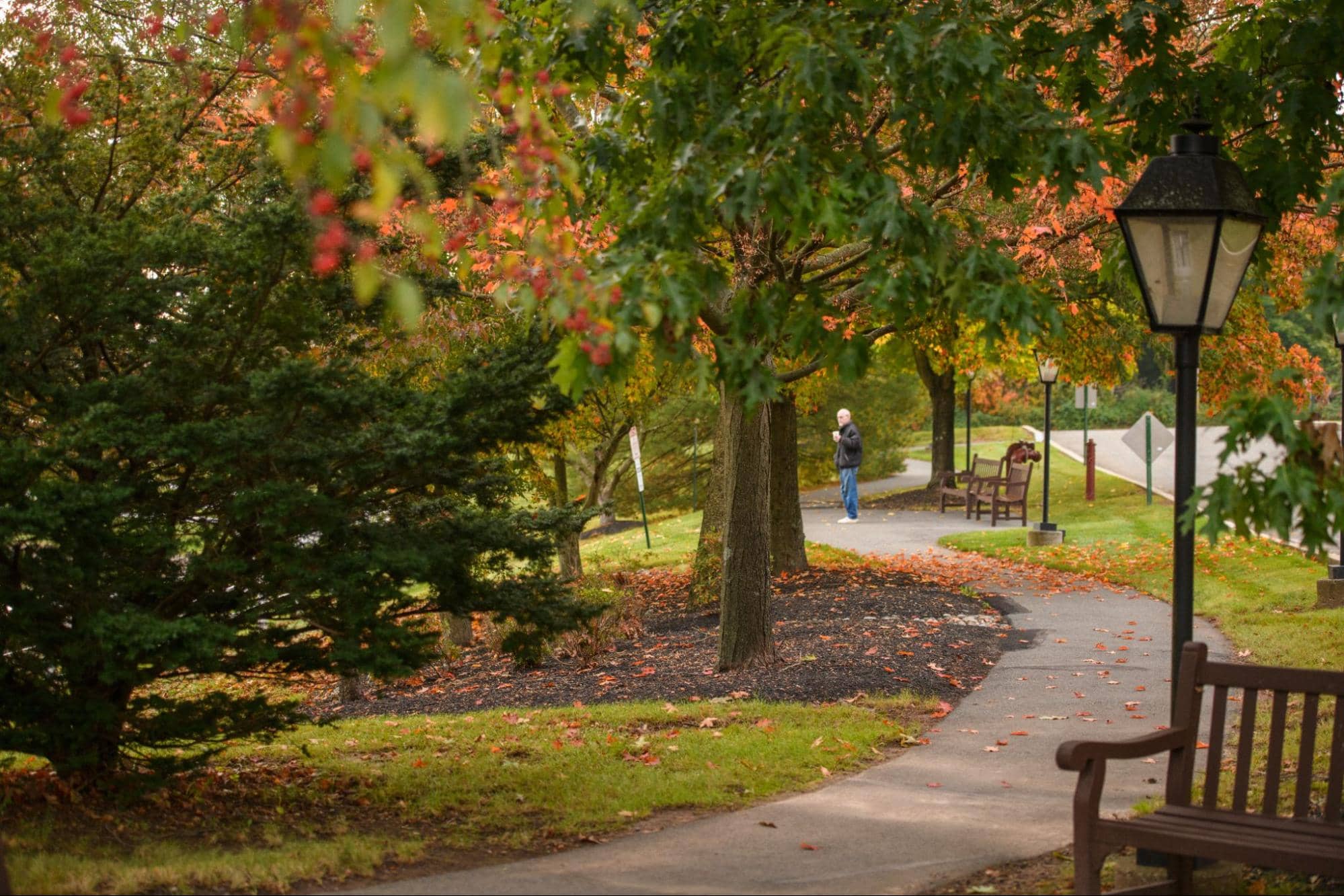 An older man enjoying a scenic autumn stroll along a paved walking path, showcasing outdoor spaces as a key example of what to look for in a retirement community.