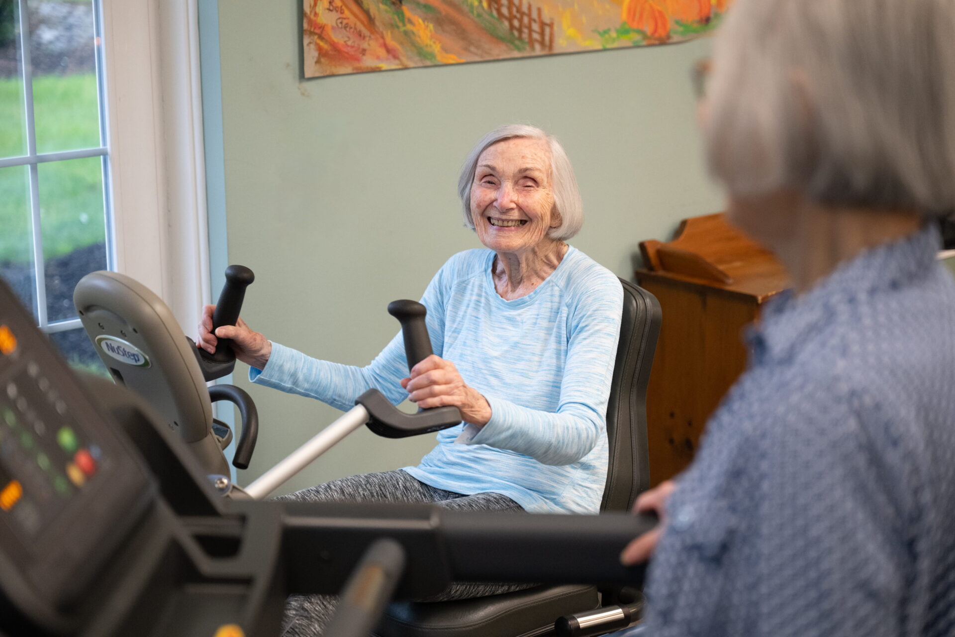 An older woman happily uses a seated stepper machine while participating in Frederick Living's rehab services program.